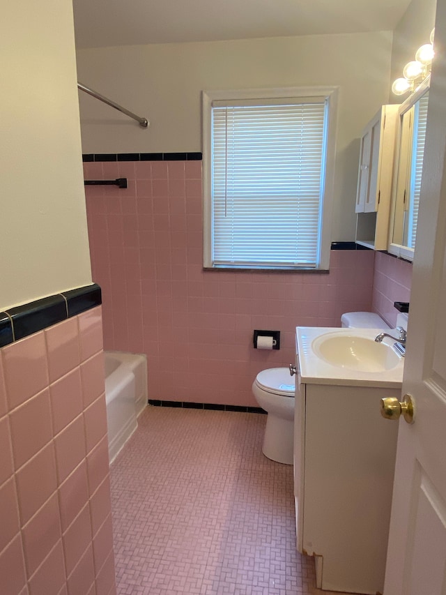 bathroom with tile walls, vanity, toilet, a wainscoted wall, and washtub / shower combination