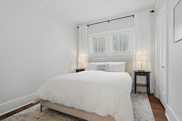 bedroom featuring a textured ceiling, dark wood-style flooring, ornamental molding, and baseboards