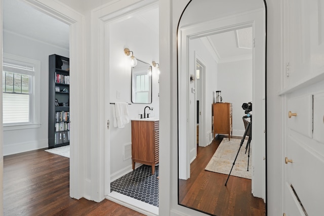 hallway with dark wood-style flooring, ornamental molding, baseboards, and a sink