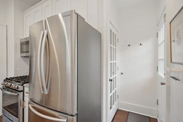 kitchen with appliances with stainless steel finishes, white cabinets, dark wood finished floors, backsplash, and baseboards
