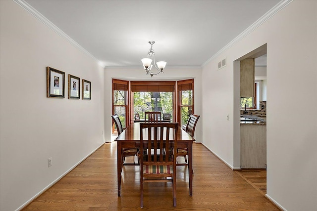 dining room featuring a chandelier, ornamental molding, light wood-style floors, and baseboards
