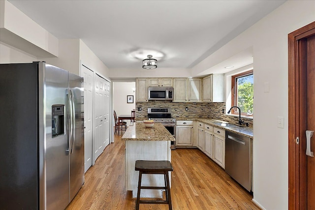 kitchen featuring appliances with stainless steel finishes, a sink, cream cabinetry, and light wood-style flooring