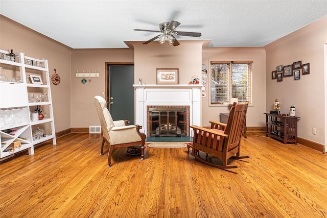 3541 Highland Blvd, Highland, MI 48356 - living area featuring a ceiling fan, a fireplace, light wood-style floors, baseboards, and a textured ceiling