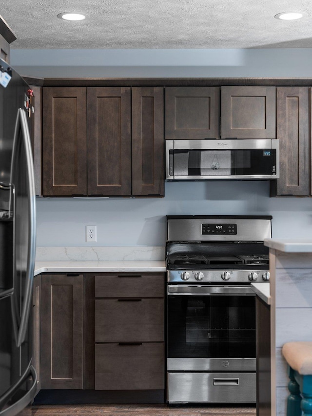 119 Maple St, Fife Lake, MI 49633 - kitchen featuring stainless steel appliances, dark brown cabinets, a textured ceiling, recessed lighting, and light stone counters