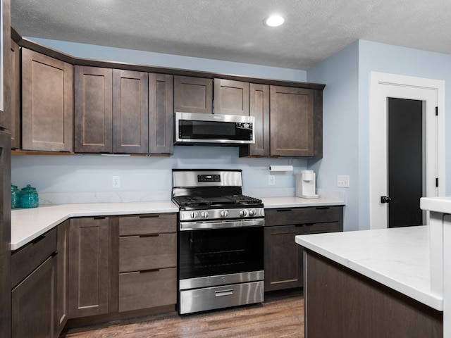 119 Maple St, Fife Lake, MI 49633 - kitchen featuring appliances with stainless steel finishes, dark brown cabinetry, wood finished floors, recessed lighting, and a textured ceiling