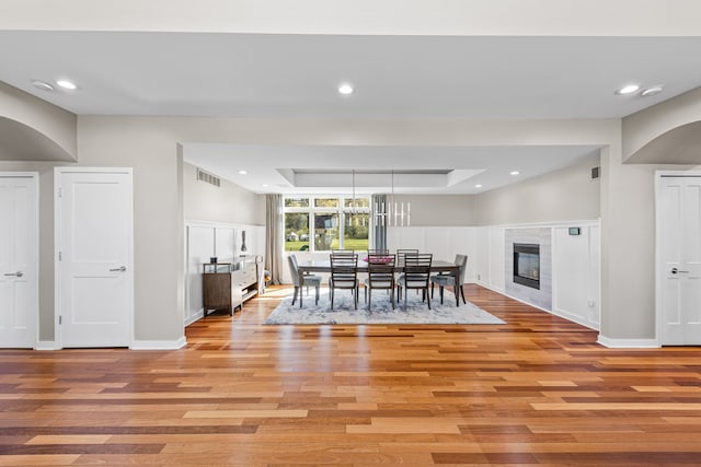 dining area featuring light wood-type flooring, a tray ceiling, baseboards, recessed lighting, and a tile fireplace