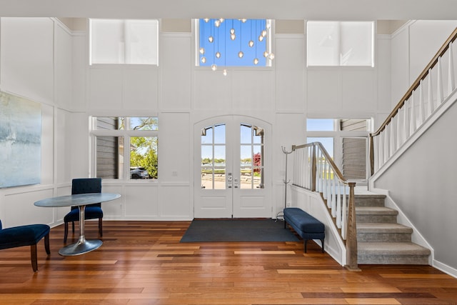 entrance foyer featuring hardwood / wood-style floors, stairs, a high ceiling, a decorative wall, and french doors