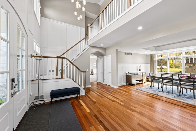 entrance foyer with arched walkways, wood finished floors, stairway, a decorative wall, and a high ceiling