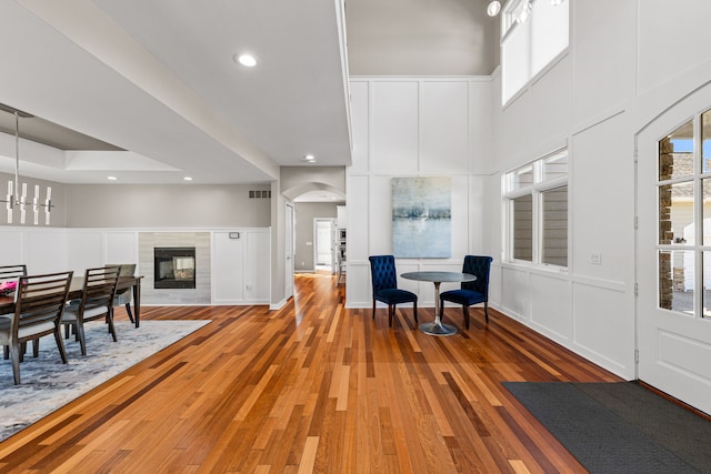 entryway with a decorative wall, arched walkways, light wood-style floors, a chandelier, and a towering ceiling