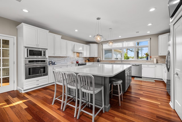 kitchen featuring appliances with stainless steel finishes, a center island, backsplash, white cabinets, and a breakfast bar area
