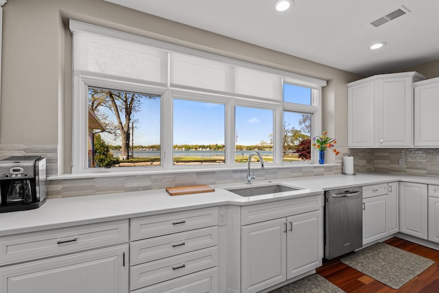 kitchen with a sink, stainless steel dishwasher, decorative backsplash, white cabinets, and light countertops