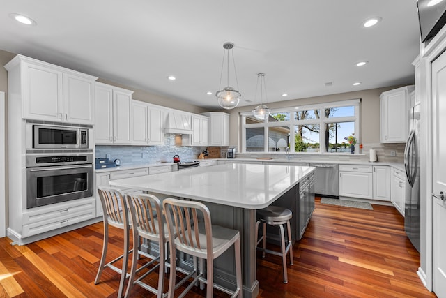 kitchen featuring stainless steel appliances, a center island, tasteful backsplash, white cabinets, and light countertops