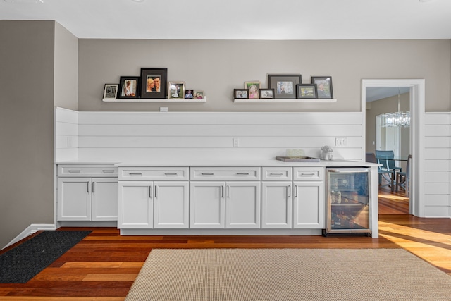 indoor bar with wine cooler, dark wood finished floors, and a chandelier