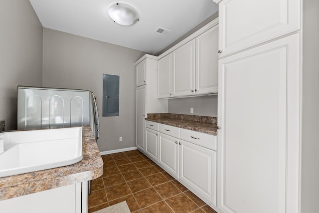 washroom with electric panel, cabinet space, baseboards, and dark tile patterned floors