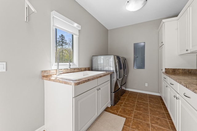 washroom with electric panel, cabinet space, separate washer and dryer, baseboards, and dark tile patterned floors