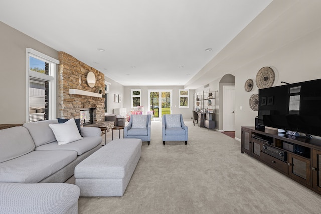 living room featuring arched walkways, a stone fireplace, healthy amount of natural light, and light carpet