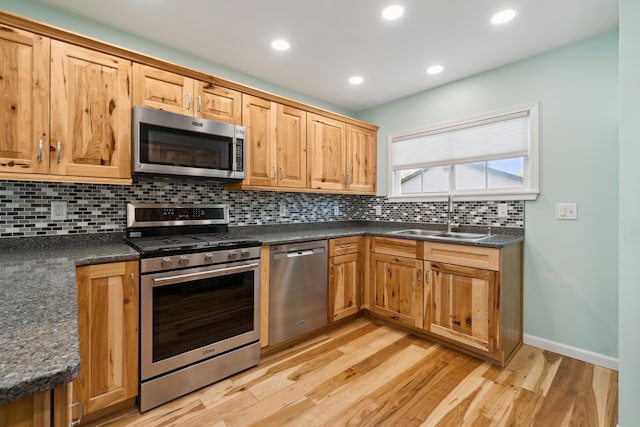 kitchen featuring stainless steel appliances, a sink, dark countertops, backsplash, and light wood finished floors