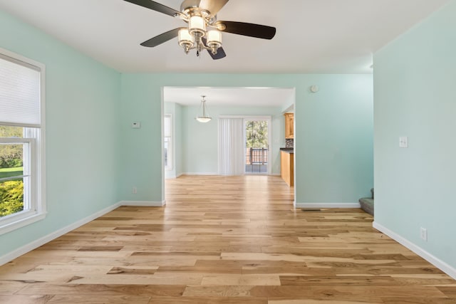 empty room featuring light wood finished floors, a ceiling fan, stairway, and baseboards