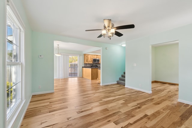 unfurnished living room with stairway, light wood finished floors, ceiling fan, and baseboards