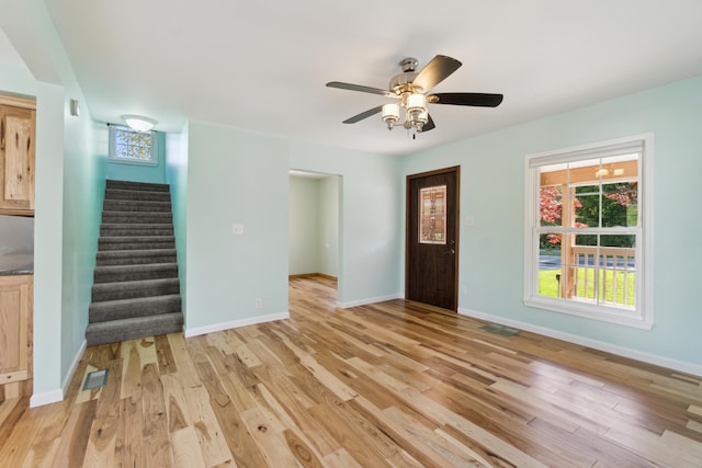 unfurnished living room featuring stairs, light wood-type flooring, and baseboards