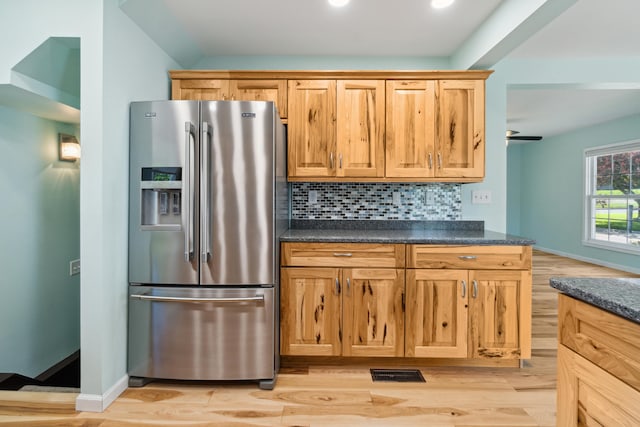 kitchen featuring stainless steel fridge with ice dispenser, dark countertops, light wood finished floors, tasteful backsplash, and baseboards