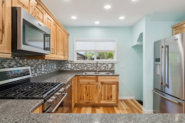 kitchen featuring stainless steel appliances, a sink, tasteful backsplash, light wood finished floors, and recessed lighting