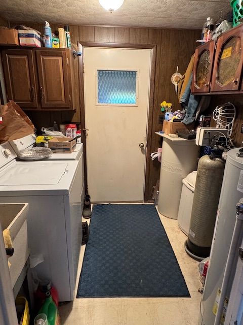 laundry area with washing machine and dryer, cabinet space, wooden walls, and gas water heater