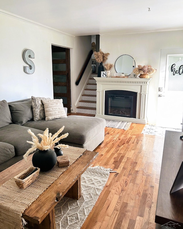 living room with crown molding, wood finished floors, stairway, and a glass covered fireplace