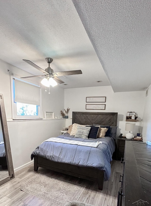 bedroom with a textured ceiling, light wood-style flooring, baseboards, and ceiling fan