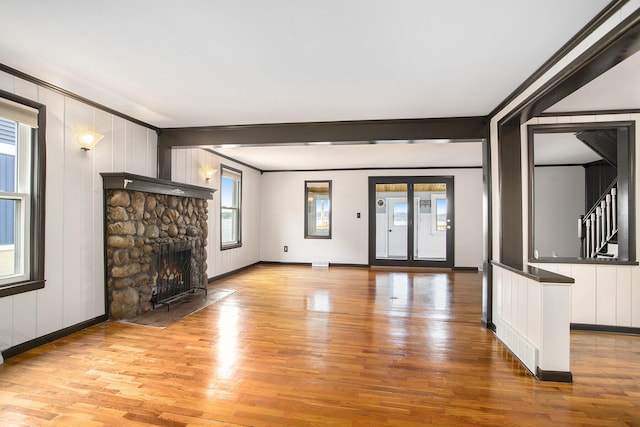 unfurnished living room with light wood finished floors, a stone fireplace, baseboards, stairs, and a decorative wall