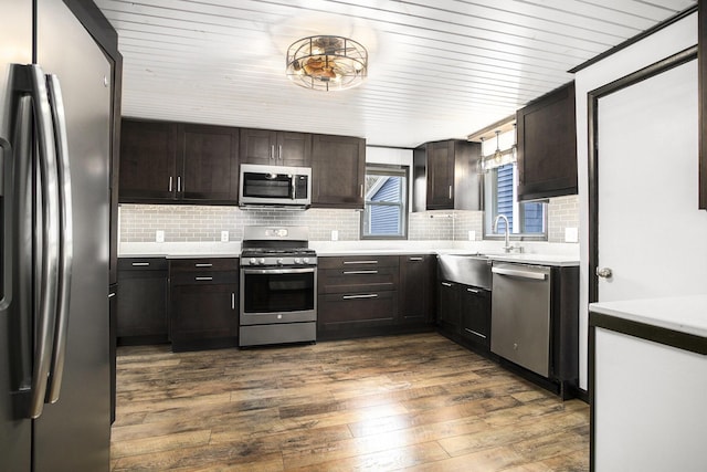 kitchen featuring appliances with stainless steel finishes, decorative backsplash, dark brown cabinets, dark wood finished floors, and light countertops