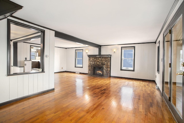 unfurnished living room featuring wood finished floors, baseboards, and a stone fireplace