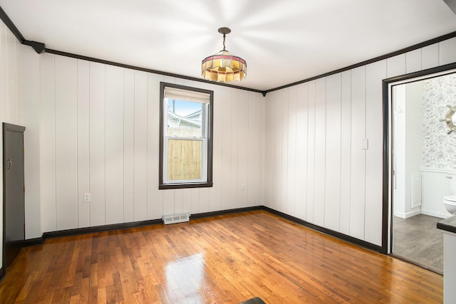 unfurnished bedroom featuring wood finished floors, crown molding, and ensuite bathroom