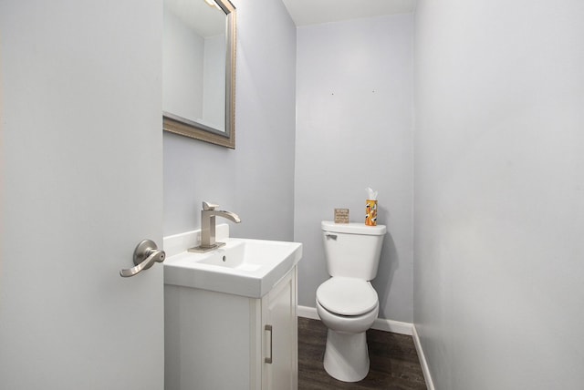 half bath with toilet, wood finished floors, vanity, and baseboards