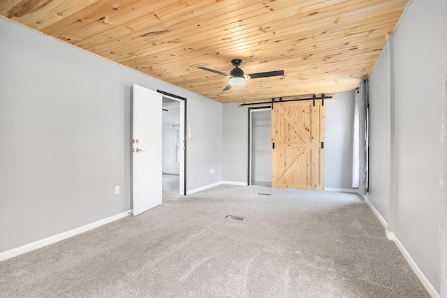 unfurnished bedroom with wood ceiling, carpet floors, a barn door, a closet, and baseboards