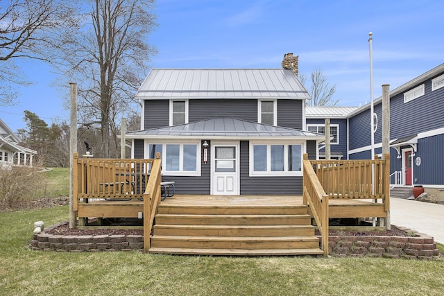back of property with a standing seam roof, metal roof, a chimney, a deck, and a yard