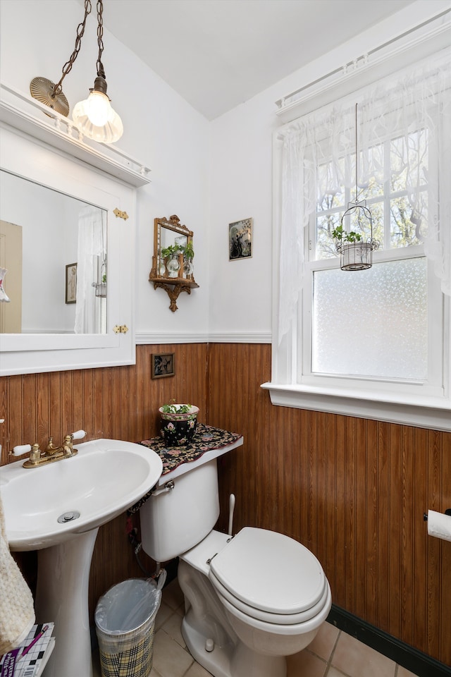 bathroom featuring wainscoting, tile patterned floors, toilet, wooden walls, and a sink