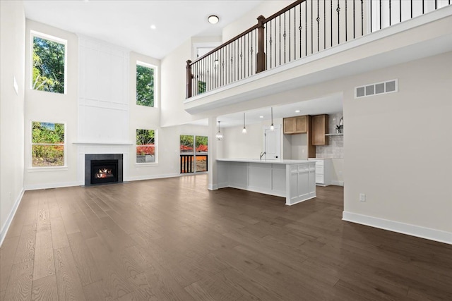 2080 Crested Butte Dr, White Lake, MI 48383 - unfurnished living room featuring a high ceiling, baseboards, dark wood-style floors, a large fireplace, and a sink