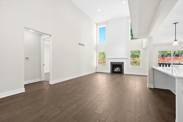 2080 Crested Butte Dr, White Lake, MI 48383 - unfurnished living room with dark wood-type flooring, a towering ceiling, baseboards, and a large fireplace
