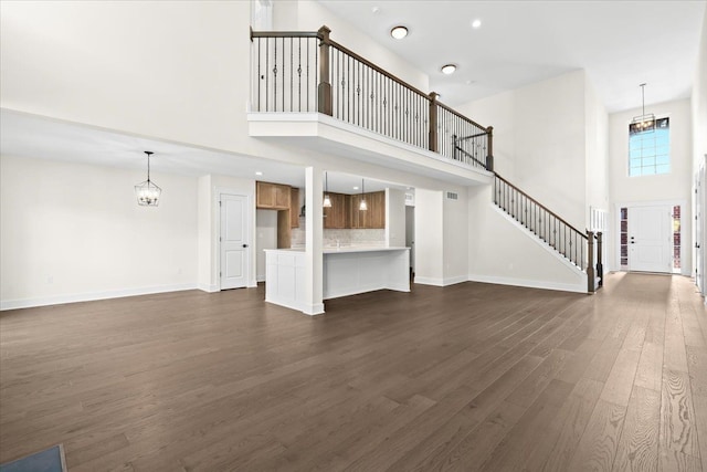 2080 Crested Butte Dr, White Lake, MI 48383 - unfurnished living room with a towering ceiling, dark wood-style floors, a chandelier, and baseboards