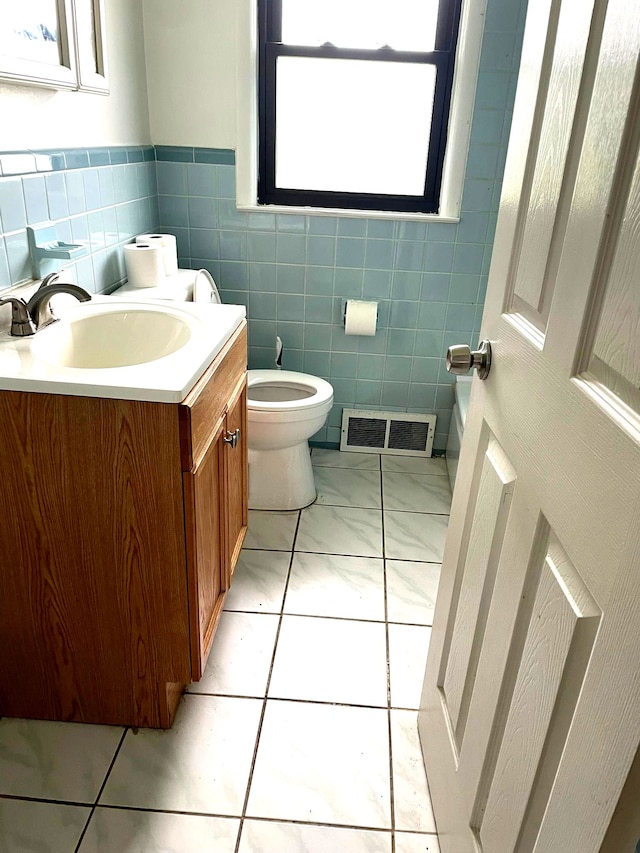 bathroom with toilet, vanity, tile walls, and wainscoting