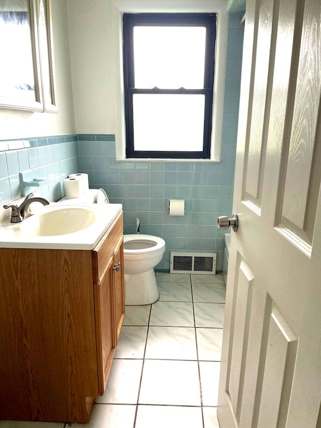 half bath with toilet, vanity, tile walls, wainscoting, and tile patterned flooring