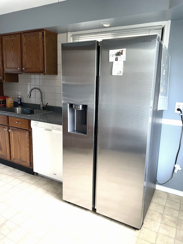 kitchen featuring dishwasher, stainless steel fridge with ice dispenser, a sink, dark countertops, and tasteful backsplash