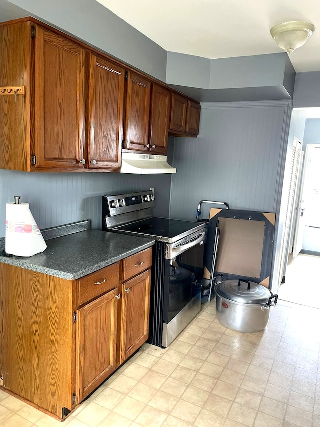 kitchen with stainless steel range with electric stovetop, under cabinet range hood, light floors, and brown cabinets
