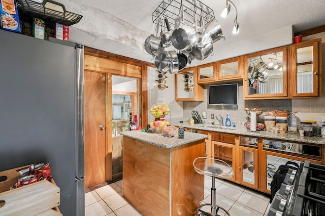 19303 Fenmore St, Detroit, MI 48235 - kitchen with freestanding refrigerator, a kitchen island, light tile patterned floors, light stone counters, and brown cabinets