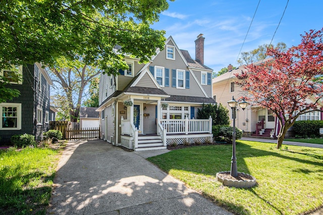 view of front of property featuring a chimney, a shingled roof, a detached garage, and covered porch