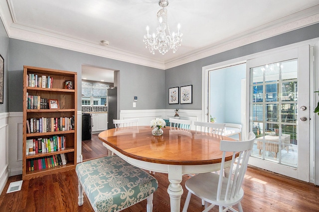 dining room with a wainscoted wall, a chandelier, healthy amount of natural light, wood finished floors, and ornamental molding