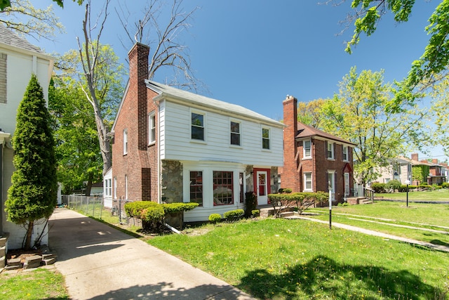 colonial inspired home with a chimney, concrete driveway, a front lawn, and a residential view