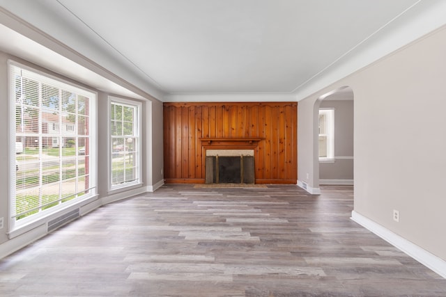 unfurnished living room with a fireplace, arched walkways, baseboards, and light wood finished floors