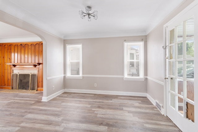 unfurnished living room with plenty of natural light, arched walkways, wood finished floors, a fireplace, and crown molding